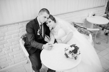 Bir kafede bir masada oturan ve el ele tutuşarak düğün çifti. B