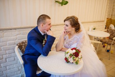 Bir kafede bir masada oturan ve el ele tutuşarak düğün çifti.