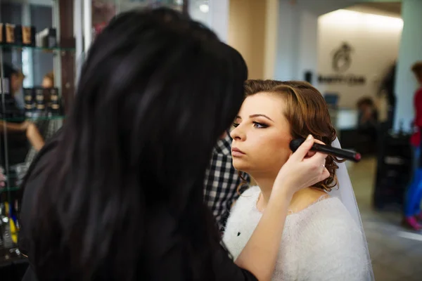Mujer joven aplicando maquillaje a modelo novia en salón de belleza . — Foto de Stock