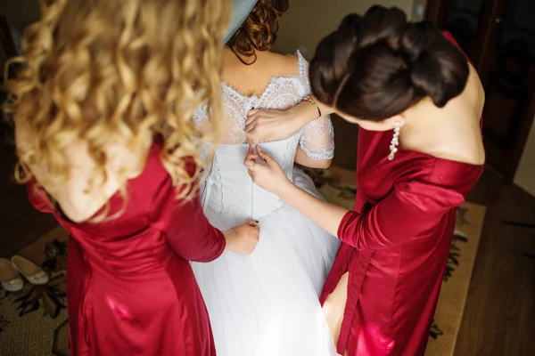 Dama de honor en vestidos rojos ayudar a la novia a vestido de novia vestido . — Foto de Stock