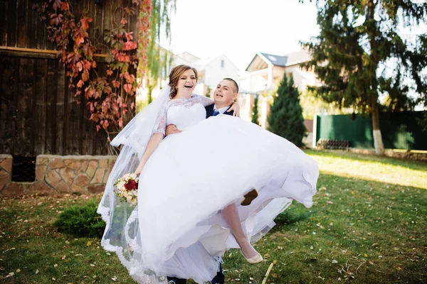 Groom tenir sur les mains mariée contre vieille maison en bois à autu ensoleillé — Photo