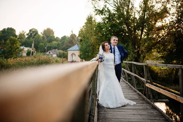 Pareja alegre boda en puente de madera al atardecer . —  Fotos de Stock