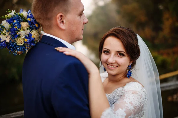 Couple de mariage joyeux sur un pont en bois au coucher du soleil . — Photo