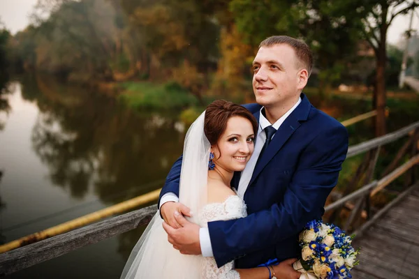 Couple de mariage joyeux sur un pont en bois au coucher du soleil . — Photo