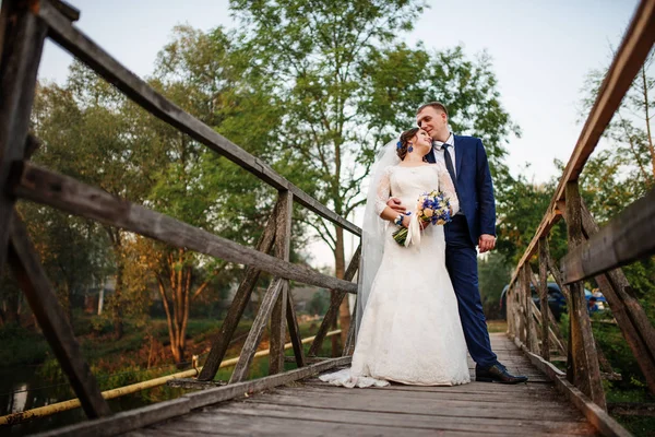 Fröhliches Hochzeitspaar auf Holzbrücke bei Sonnenuntergang. — Stockfoto