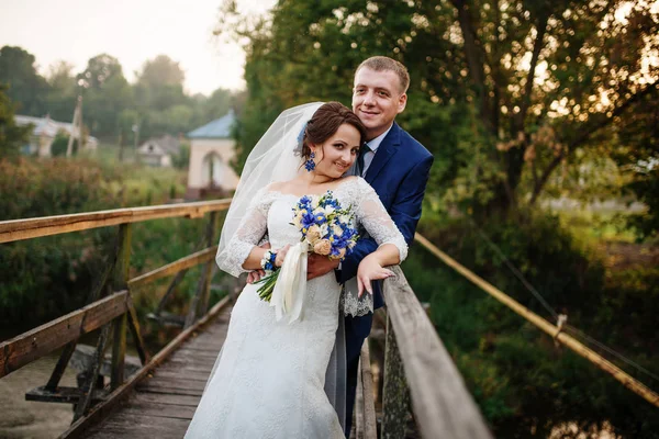 Couple de mariage joyeux sur un pont en bois au coucher du soleil . — Photo