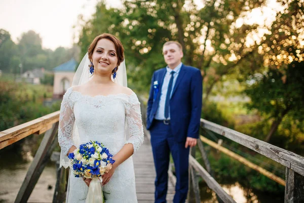 Veselé svatební pár na dřevěný most při západu slunce. — Stock fotografie