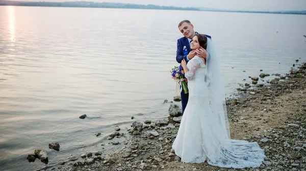 Recién casados enamorados cerca del río en la puesta del sol en su boda impresionante —  Fotos de Stock