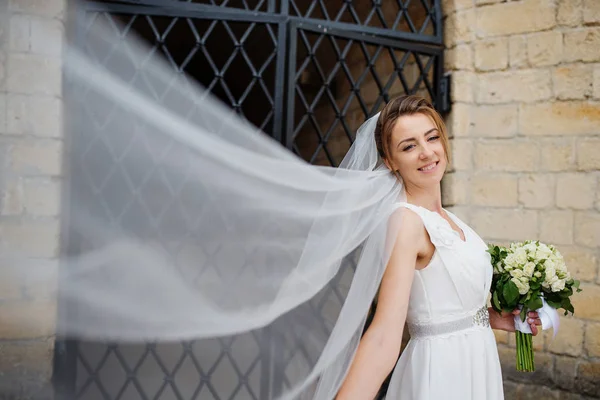 Bride with long veil near old wrought iron gates.