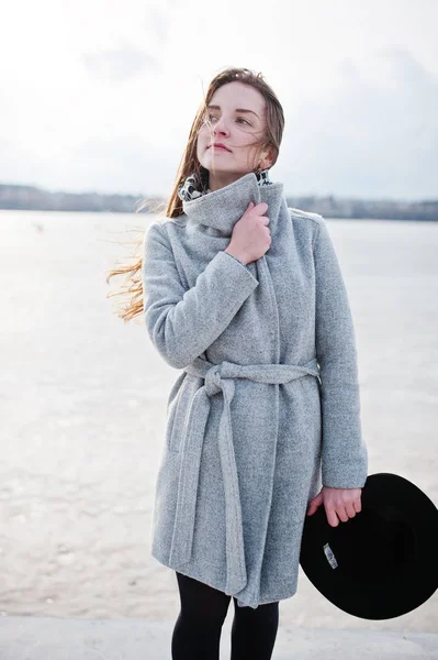 Jeune fille modèle en manteau gris et chapeau noir posé contre freez — Photo