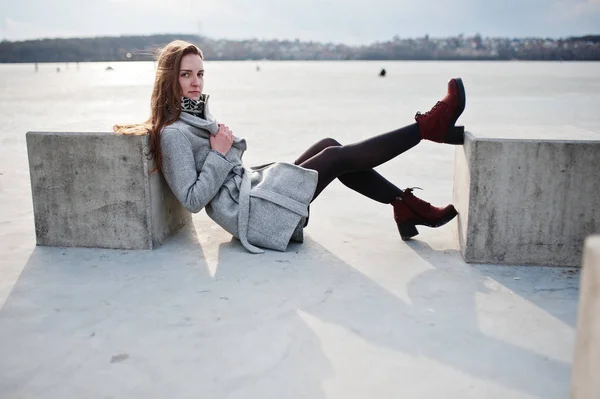 Young model girl in gray coat posed sitting near stone cube agai — Stock Photo, Image