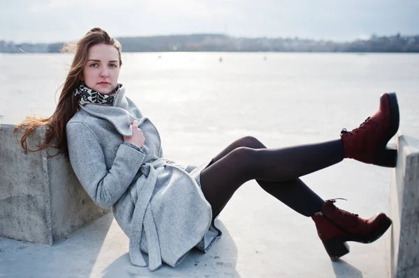 Jovem modelo menina em casaco cinza posou sentado perto de pedra cubo agai — Fotografia de Stock
