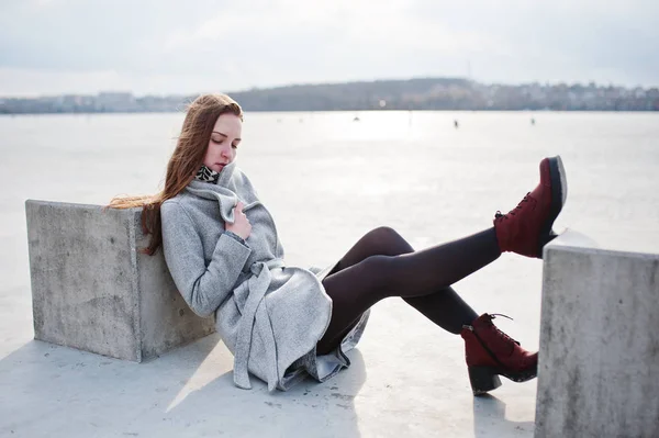 Chica modelo joven en abrigo gris posado sentado cerca de piedra cubo agai — Foto de Stock