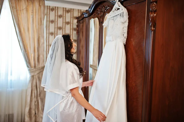 Brunette bride in a bathrobe with dress on hotel room at morning — Stock Photo, Image