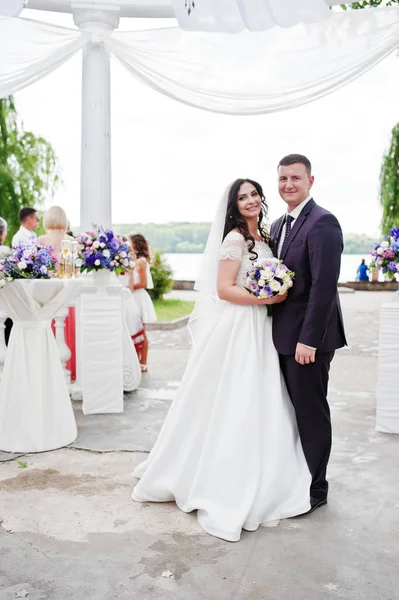 Matrimonio coppia posato sotto arco bianco alla cerimonia di nozze . — Foto Stock