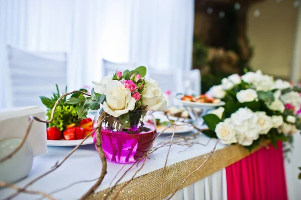 Květiny na vázu s růžovou vodou u stolu novomanželé. — Stock fotografie
