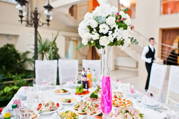 Blommor på vas med rosa vatten vid bordet av bröllopsgäster. — Stockfoto