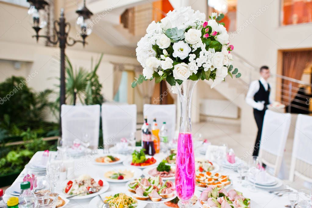 Flowers on vase with pink water at table of wedding guests.
