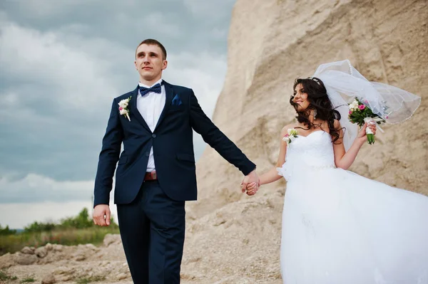 Jonge stijlvolle bruidspaar tegen zandstrand carrière bij bewolkte hemel. — Stockfoto