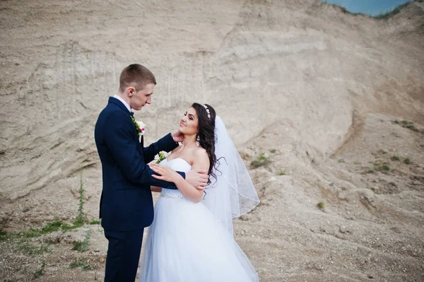 Молодая стильная свадебная пара против песчаной карьеры на облачном небе . — стоковое фото