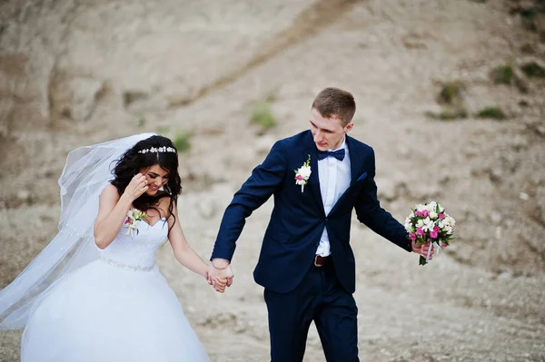 Joven pareja de boda con estilo contra la carrera arenosa en el cielo nublado . — Foto de Stock