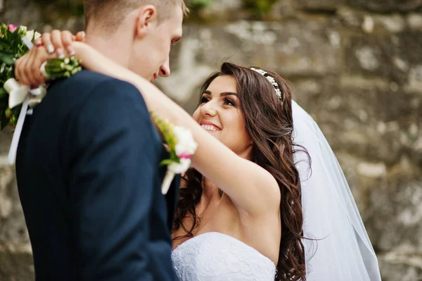 Young stylish wedding couple against old stone wall. — Stock Photo, Image