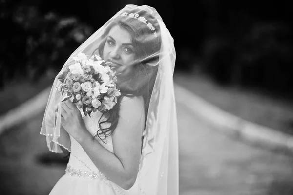 Charming brunette bride under veil with bouquet at park. Black a — Stock Photo, Image