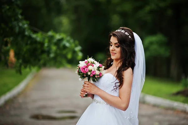 Charmante brünette Braut mit Blumenstrauß im Park. — Stockfoto