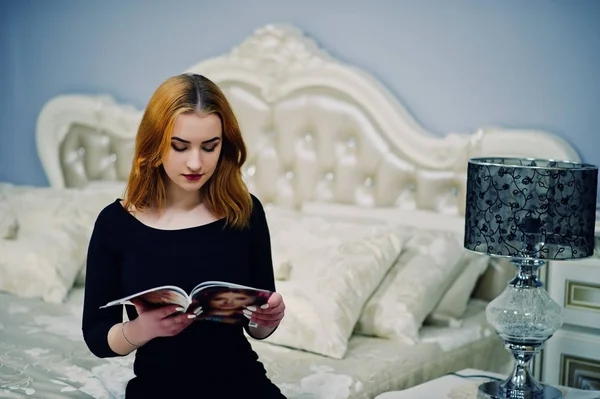 Rudowłosy dziewczyna w czarnej sukni, siedząc na łóżku i czytanie m — Zdjęcie stockowe