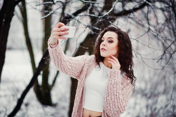 Menina morena encaracolado com telefone celular na mão fazendo selfie de volta — Fotografia de Stock
