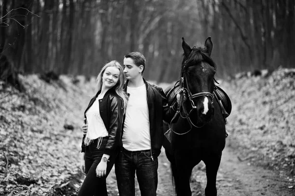 Casal elegante jovem no amor perto de cavalo em floresta de outono. Preto. — Fotografia de Stock