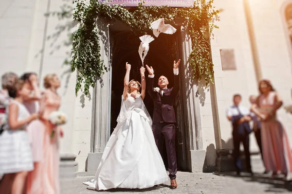 Hochzeitspaar lässt Tauben gegen Kirche in den Himmel steigen — Stockfoto