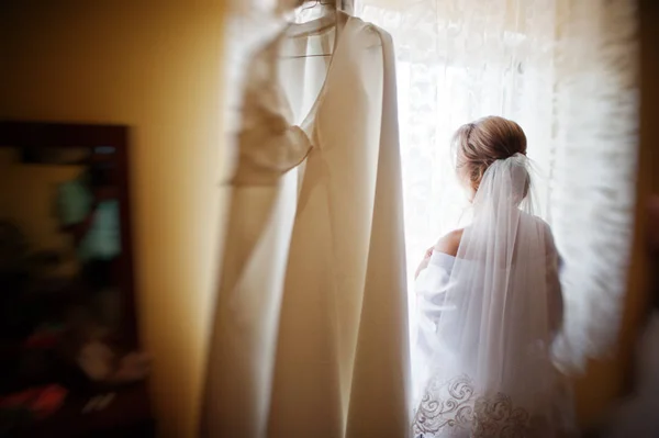 Bruid zijden kleed kijken op venster met trouwjurk op kamer — Stockfoto