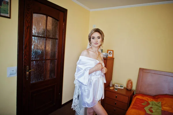 Noiva em robe de seda olhando na janela no quarto no dia da manhã . — Fotografia de Stock