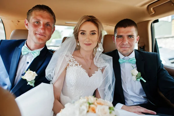 Bride sitting at the back seat of luxury wedding car with two be