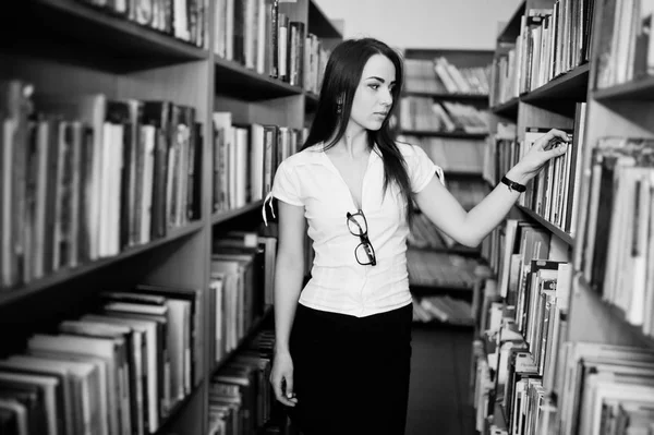 Μελαχρινή κοπέλα σε βιβλιοθήκη, φορούν λευκή μπλούζα και μαύρη μίνι sk — Φωτογραφία Αρχείου