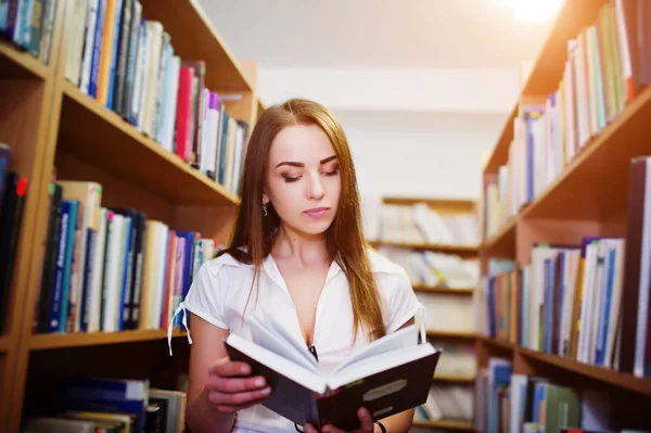 Chica morena en la biblioteca leer un libro, usar en blusa blanca y b —  Fotos de Stock