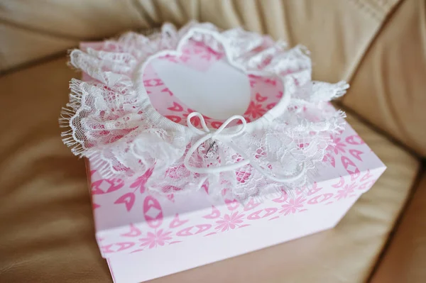 White wedding garter on rose box at leather sofa. — Stock Photo, Image