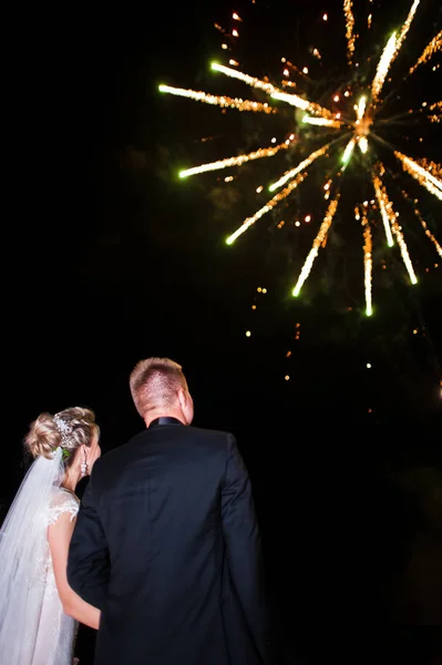 Zadní strana svatební pár při pohledu na noční oblohu s ohňostrojem. — Stock fotografie