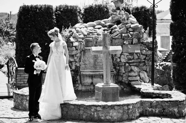 Stylish wedding couple near cross with fountain. — Stock Photo, Image