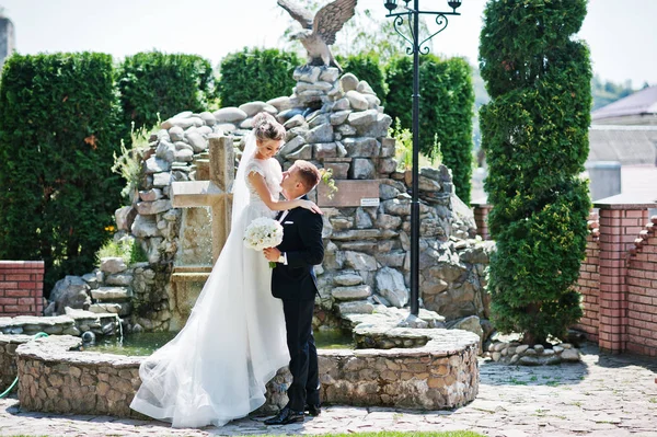 Stylish wedding couple near cross with fountain. — Stock Photo, Image