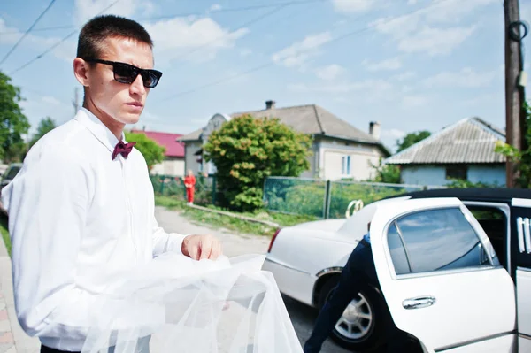 Stylish best man on sunglasses against wedding limousine.