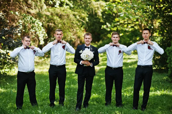 Fashionable groom with four best mans at bow ties outdoor.