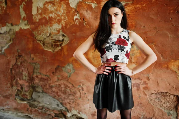 Young goth girl on black leather skirt posed against grunge wall