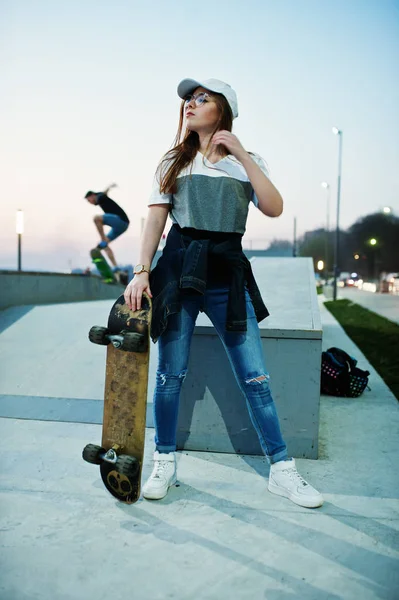 Молода дівчина-підліток міська зі скейтбордом, одягнена в окуляри, шапка — стокове фото