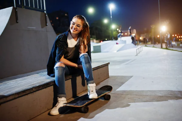Молода дівчина-підліток міська зі скейтбордом, одягнена в окуляри, шапка — стокове фото
