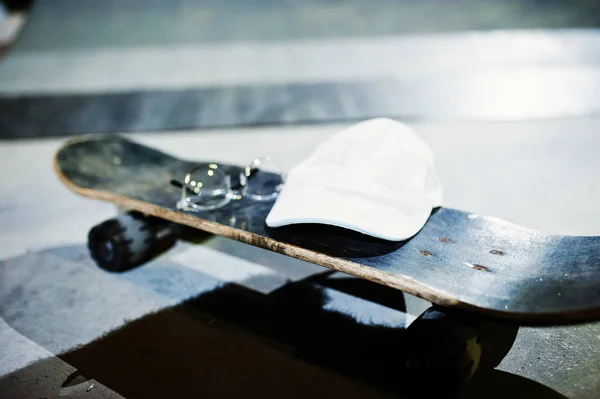 Skateboard with glasses and cap on skate park at evening. — Stock Photo, Image