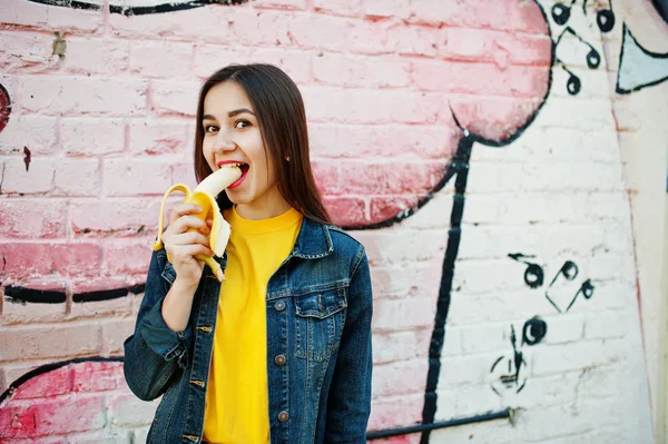 Beautiful teenage girl eat banana, wear yellow t-shirt, jeans ne