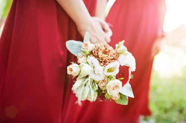 Mãos de duas damas de honra usam no vestido vermelho com buquês de casamento — Fotografia de Stock