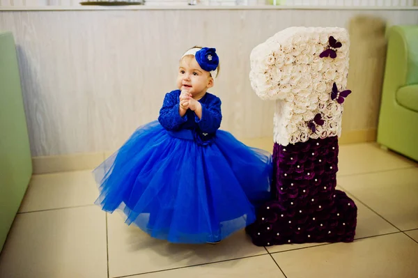 Söt liten baby flicka i blå klänning nära 1 år födelsedag nummer. — Stockfoto